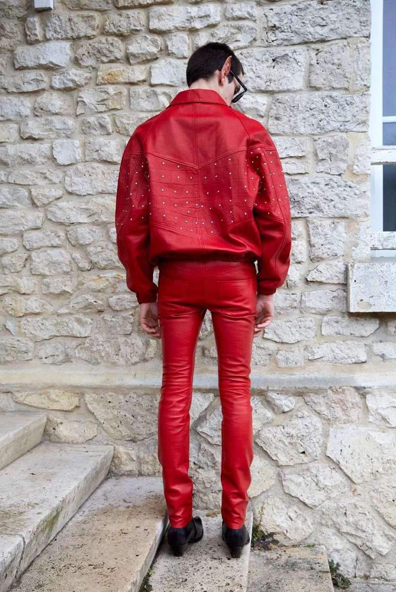 Rear view of an adult male standing on concrete steps wearing a bright red leather jacket and pants with black shoes, outdoors.