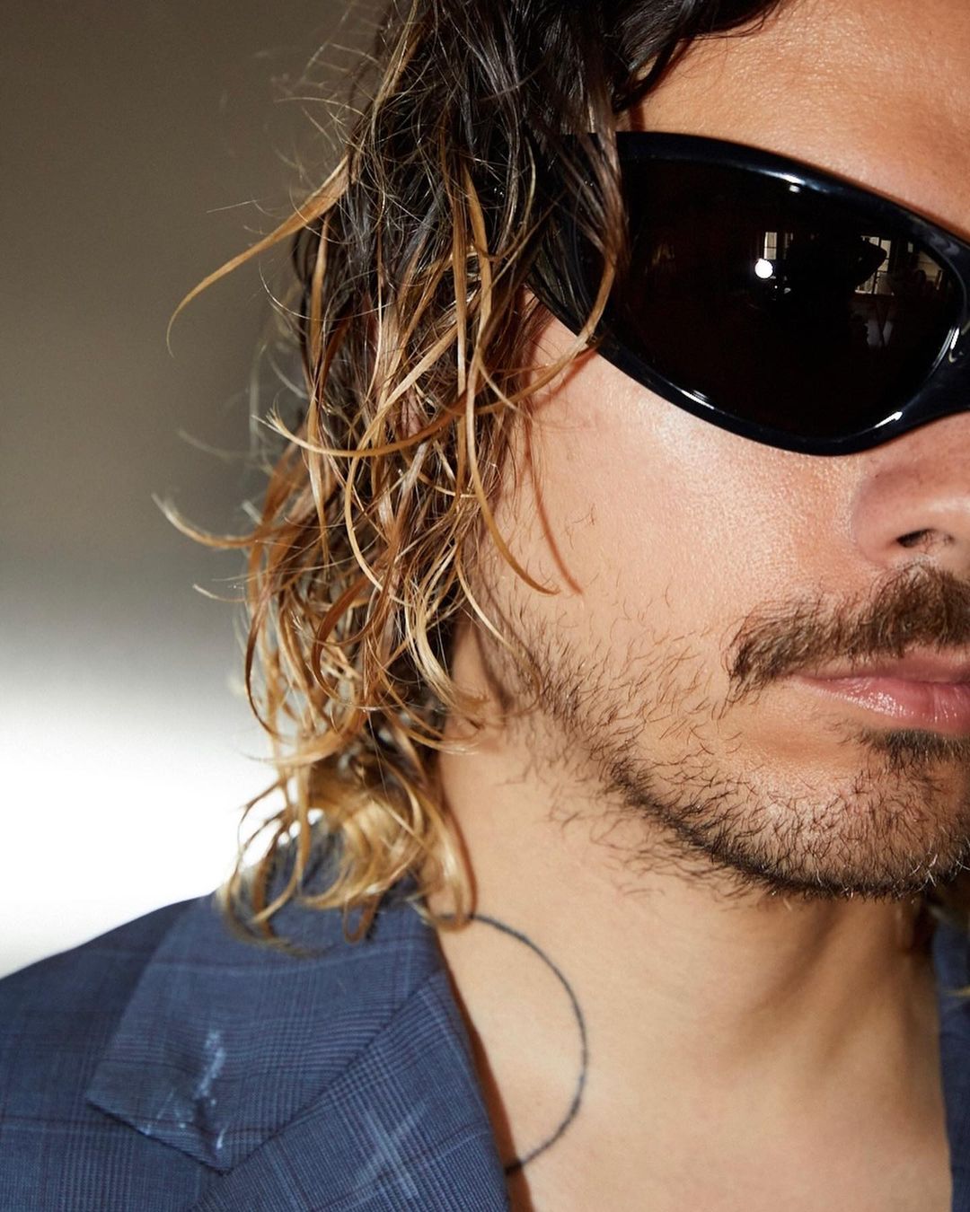 Close-up of a person wearing black sunglasses and a blue blazer, showcasing their facial features and fashion style in indoor lighting.