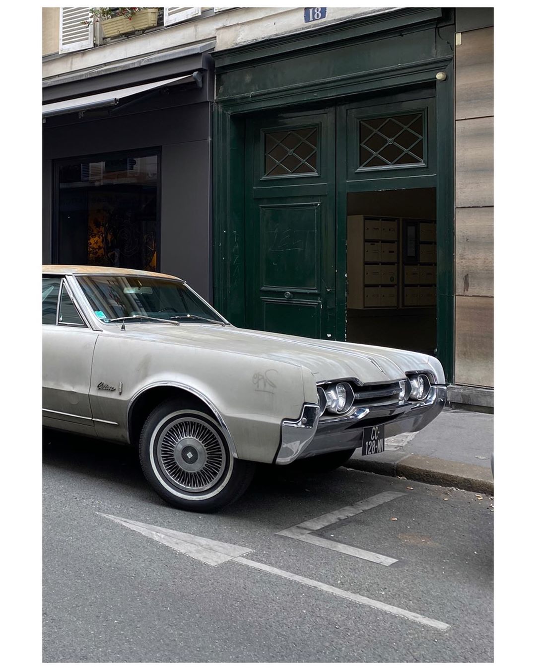 Silver vintage car parked on a city street near a building with green doors and an arrow painted on the asphalt.