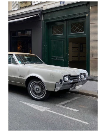Silver vintage car parked on a city street near a building with green doors and an arrow painted on the asphalt.