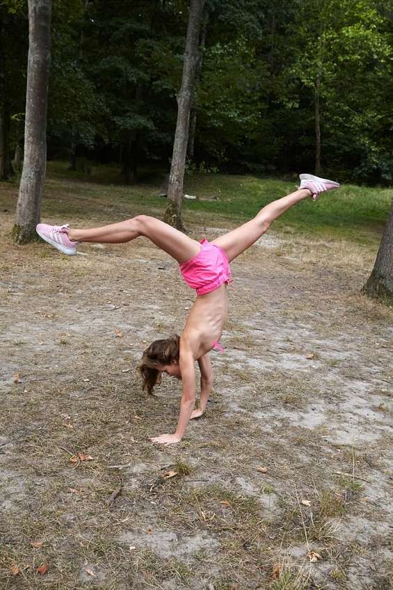 Adult female doing a handstand with legs in a V-split wearing a pink sports outfit outdoors in a forest setting.