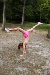 A person doing a handstand split in a woodland park, wearing pink shorts and trainers.