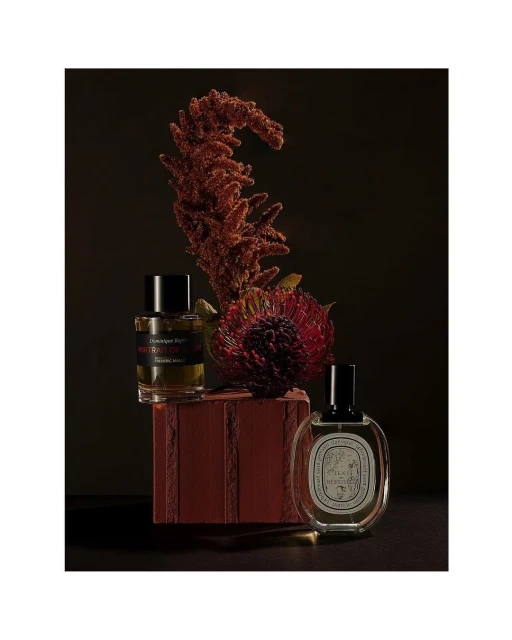 Two perfume bottles, one with a red label, and floral arrangements displayed on a red textured block against a dark background.