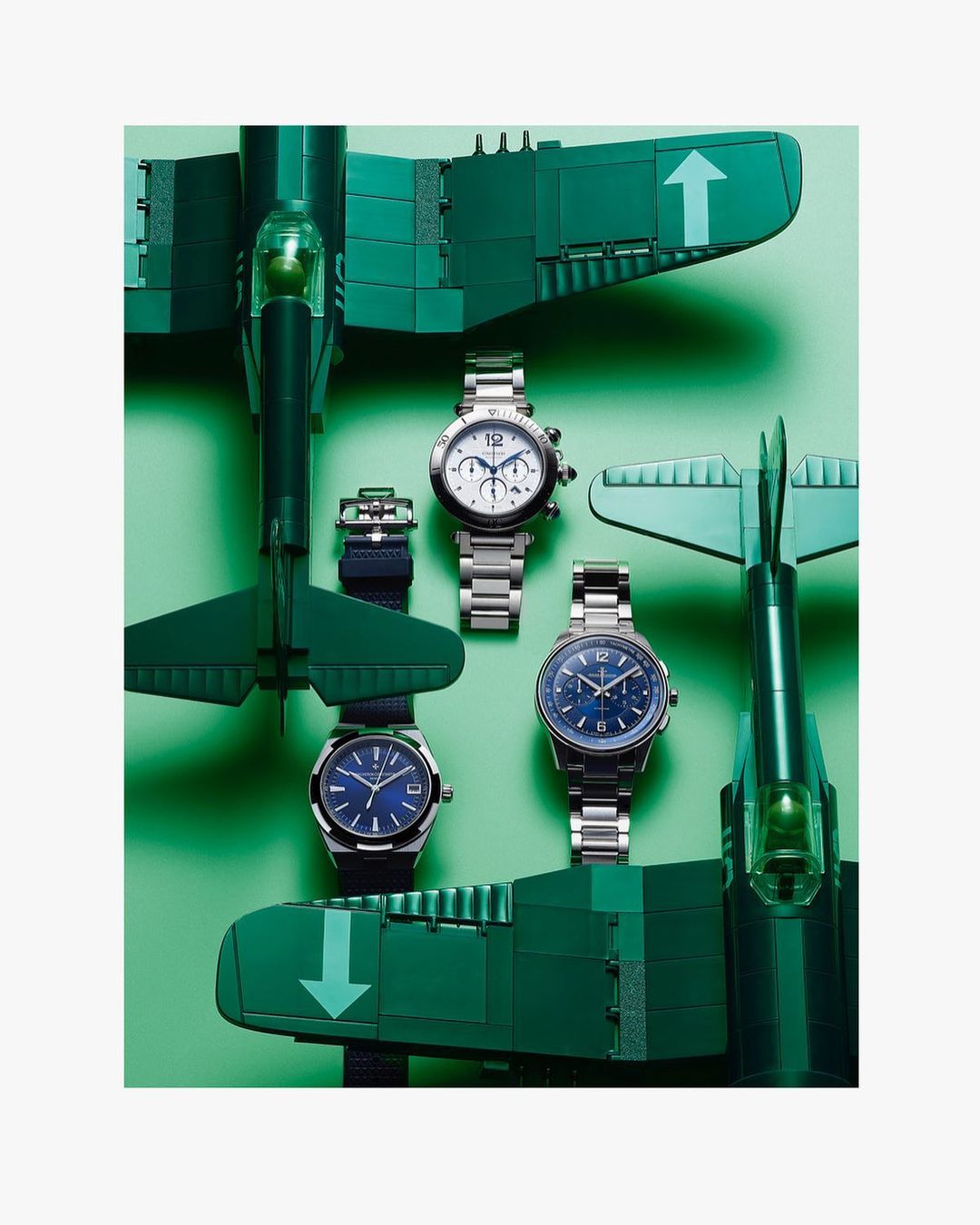 Three wristwatches with metal bands, displayed amidst toy airplanes on a light green surface, creating a visually appealing product arrangement.