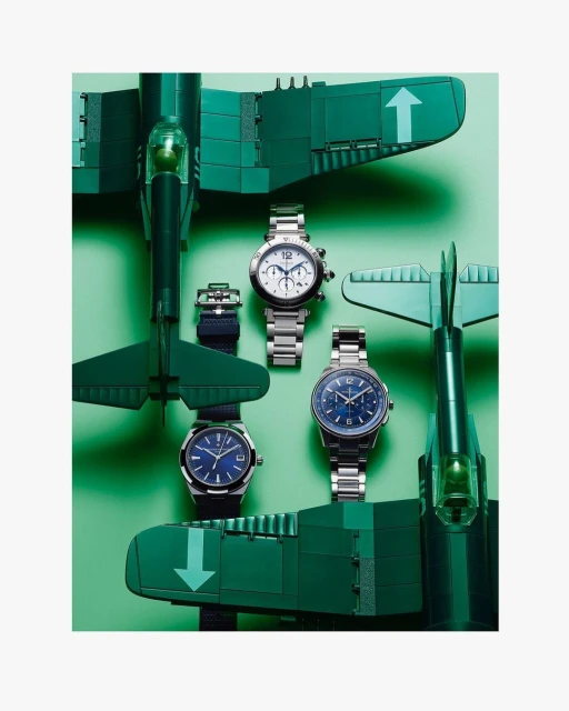 Three wristwatches with metal bands, displayed amidst toy airplanes on a light green surface, creating a visually appealing product arrangement.