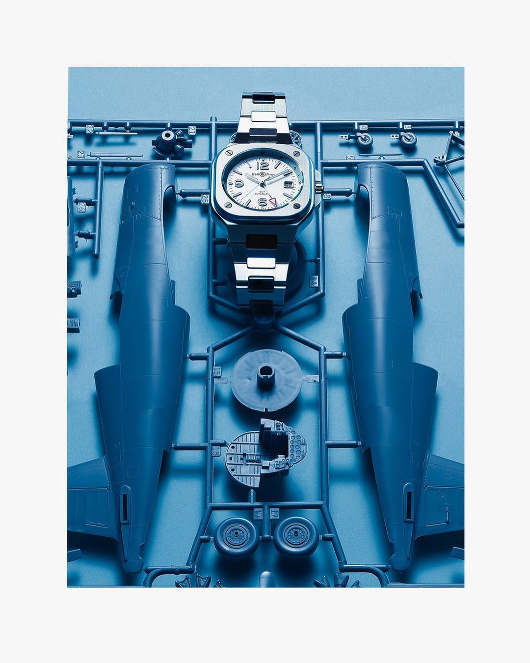 Silver wristwatch on a blue plastic airplane model kit featuring airplane body parts and accessories, set against a white background.