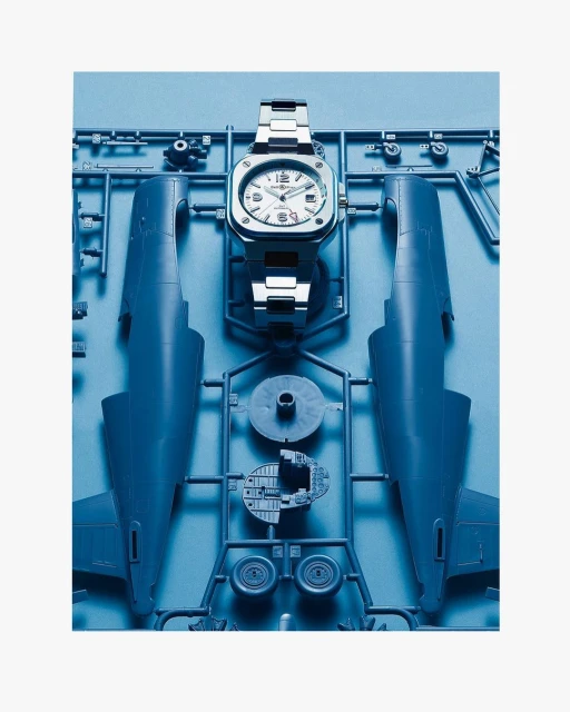 Silver wristwatch on a blue plastic airplane model kit featuring airplane body parts and accessories, set against a white background.