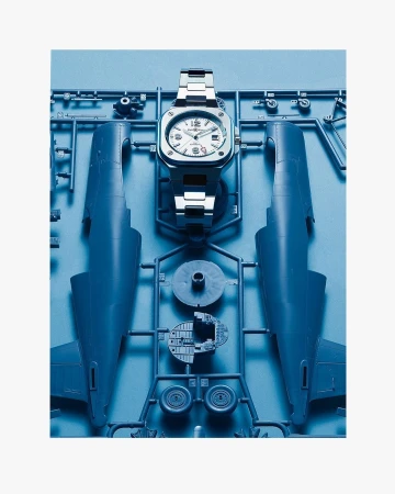 Silver wristwatch on a blue plastic airplane model kit featuring airplane body parts and accessories, set against a white background.