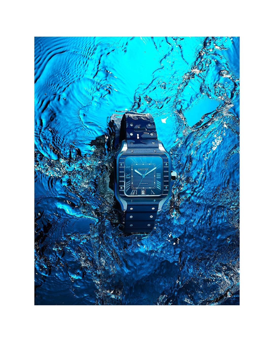 Close-up of a stainless steel wristwatch surrounded by flowing water, set against a bright blue backdrop. Product photography.