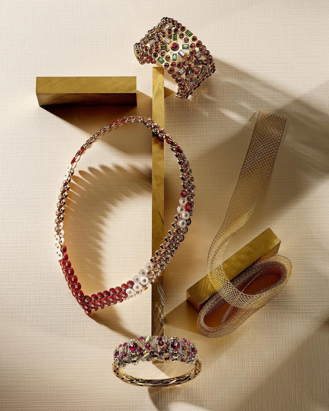 Jewelry still life: A collection of glittering necklaces and bracelets are arranged on a gold display against a textured cream backdrop.