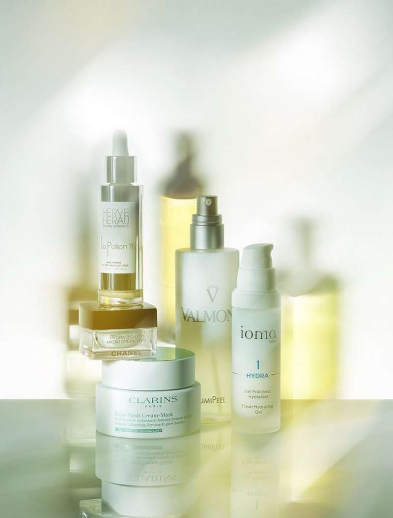 Several skincare products are displayed with labels from brands like Clarins, Chanel, and Valmont against a soft, light background.