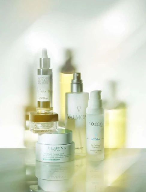 Several skincare products are displayed with labels from brands like Clarins, Chanel, and Valmont against a soft, light background.