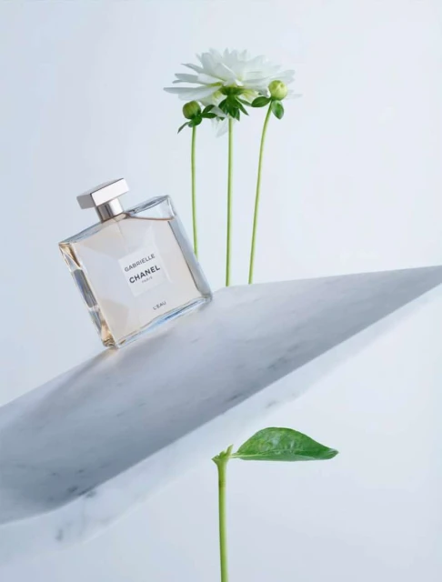 Studio shot of Chanel perfume bottle on marble surface with white flower against a clean white background, fragrance bottle, studio lighting.