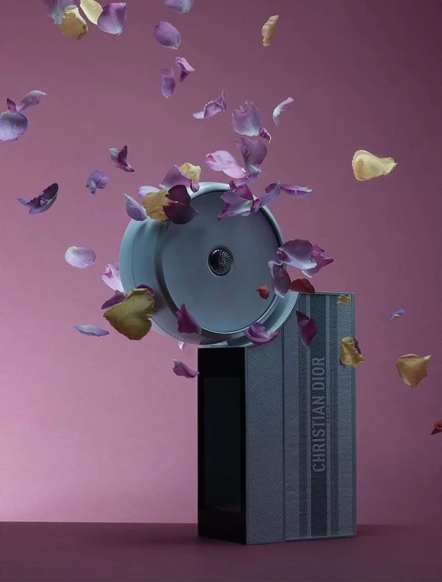 Still life featuring a gray perfume bottle and box amidst falling pink and gold petals, set against a pink background for a beauty shot.