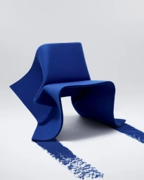 A sculptural royal blue felt chair sits against a plain white background, with blue brushstrokes extending onto the floor surface.