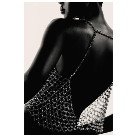 Back view of a woman wearing a metal mesh top, posing in front of a neutral backdrop, emphasizing fashion and minimalist style.