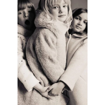 A black-and-white portrait features three young girls in winter coats, two embracing, one making an open-mouthed expression. 