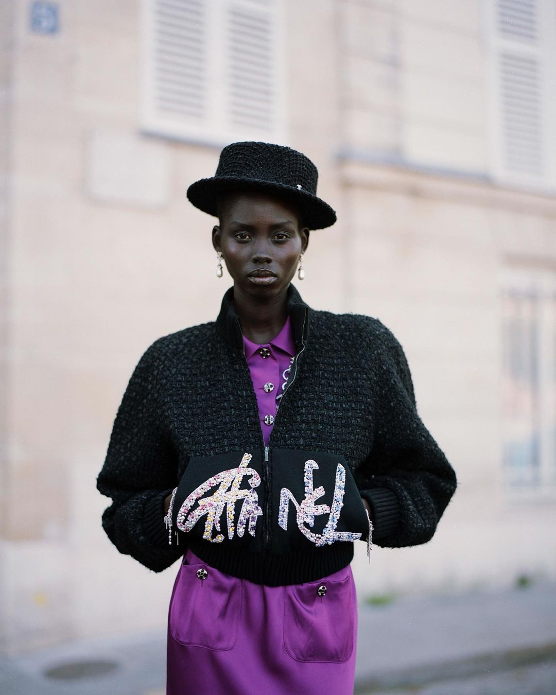 Black woman wearing a black tweed jacket, matching hat, and purple dress photographed by Fanny Latour-lambert
