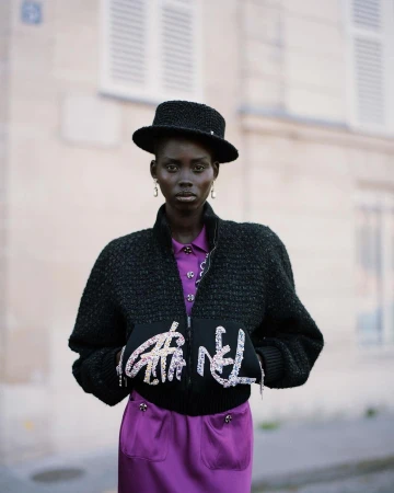 Black woman wearing a black tweed jacket, matching hat, and purple dress photographed by Fanny Latour-lambert