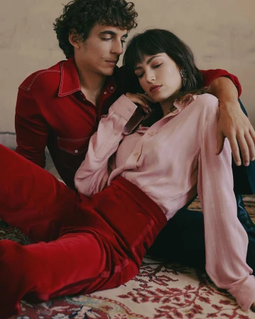 Portrait of a man in a red shirt and woman in a pink blouse seated together on a patterned carpet.