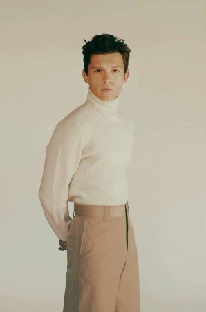 Tom Holland in a cream turtleneck sweater and khaki trousers against a seamless neutral background