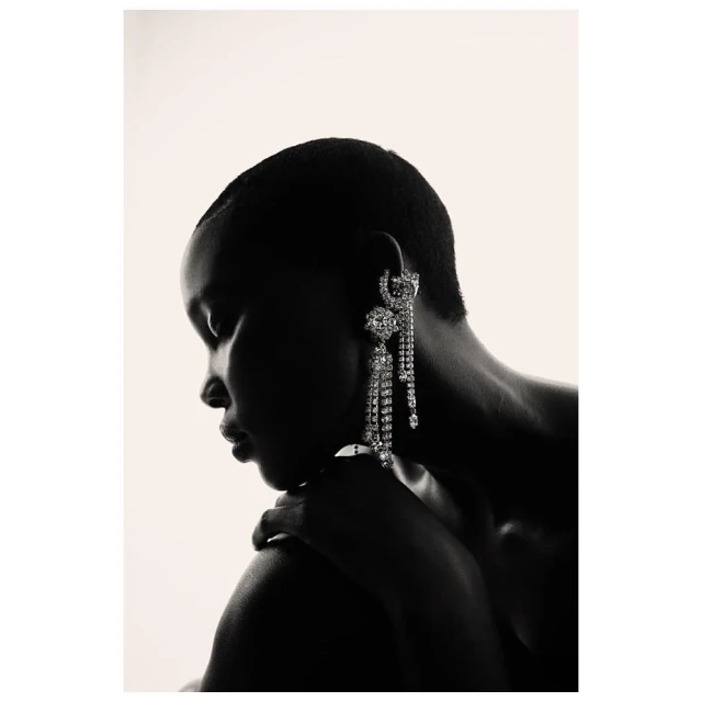 Portrait of an adult female with short dark hair, wearing a jeweled earring and ring against a white background.