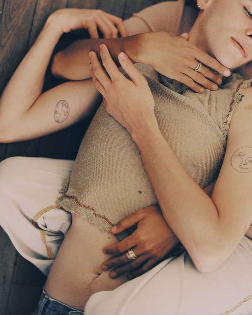 Close-up of two people intertwined, showing arms and torso, with arms wrapped around each other on a wood floor, wearing neutral colors.