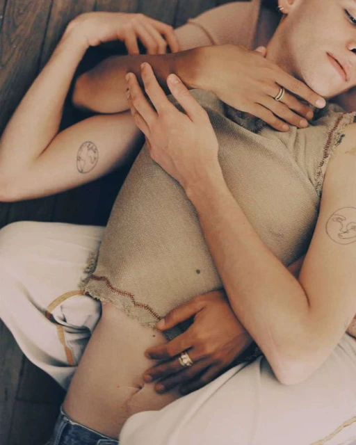 Close-up of two people intertwined, showing arms and torso, with arms wrapped around each other on a wood floor, wearing neutral colors.