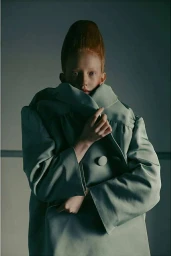 Model with sculpted red hair wearing a sage green oversized coat pulled high around neck by photographer Fanny Latour-lambert