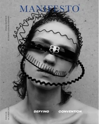 Close-up portrait of a model wearing sunglasses and a wire crown accessory against a concrete wall