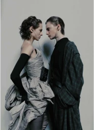 Two women standing face to face sharing earphones while wearing contrasting grey gown and dark plaid coat by Fanny Latour-lambert