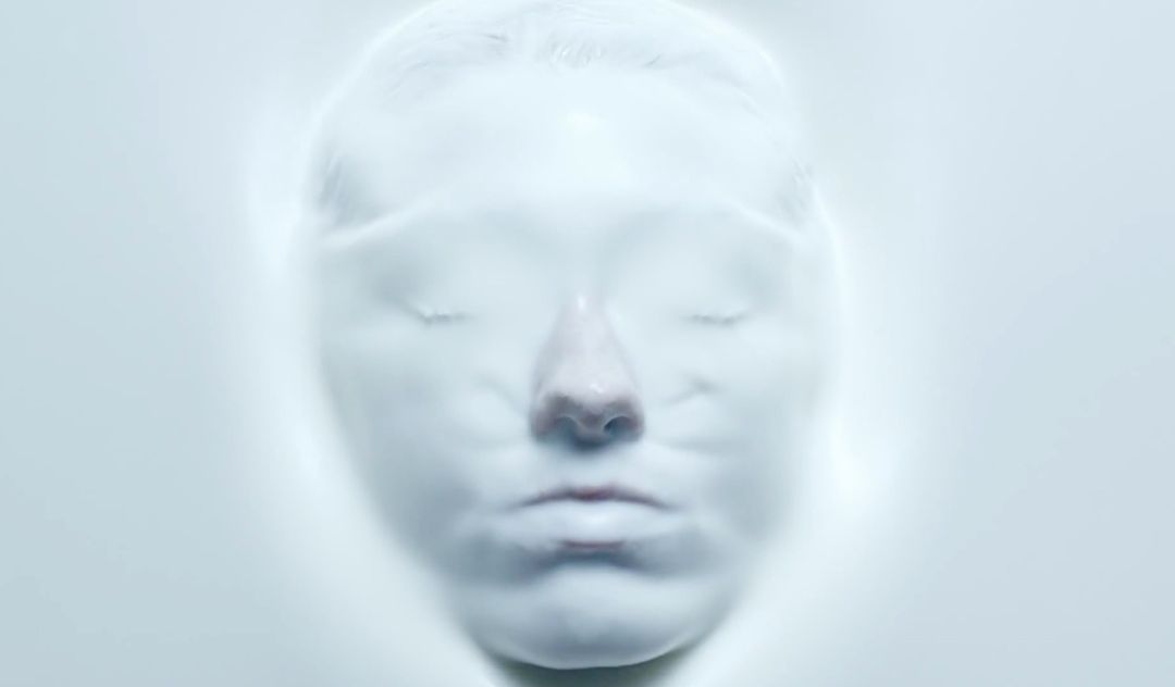Abstract beauty portrait of a serene adult female face covered in opaque white fluid, eyes closed, minimal lighting, cool color palette.