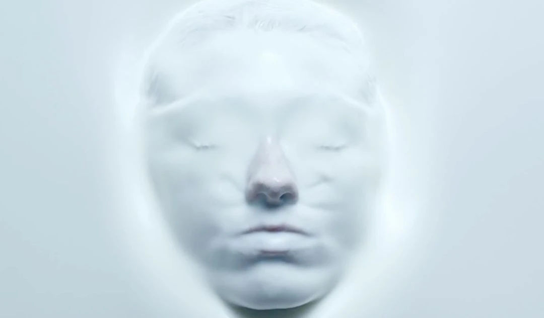 Abstract beauty portrait of a serene adult female face covered in opaque white fluid, eyes closed, minimal lighting, cool color palette.