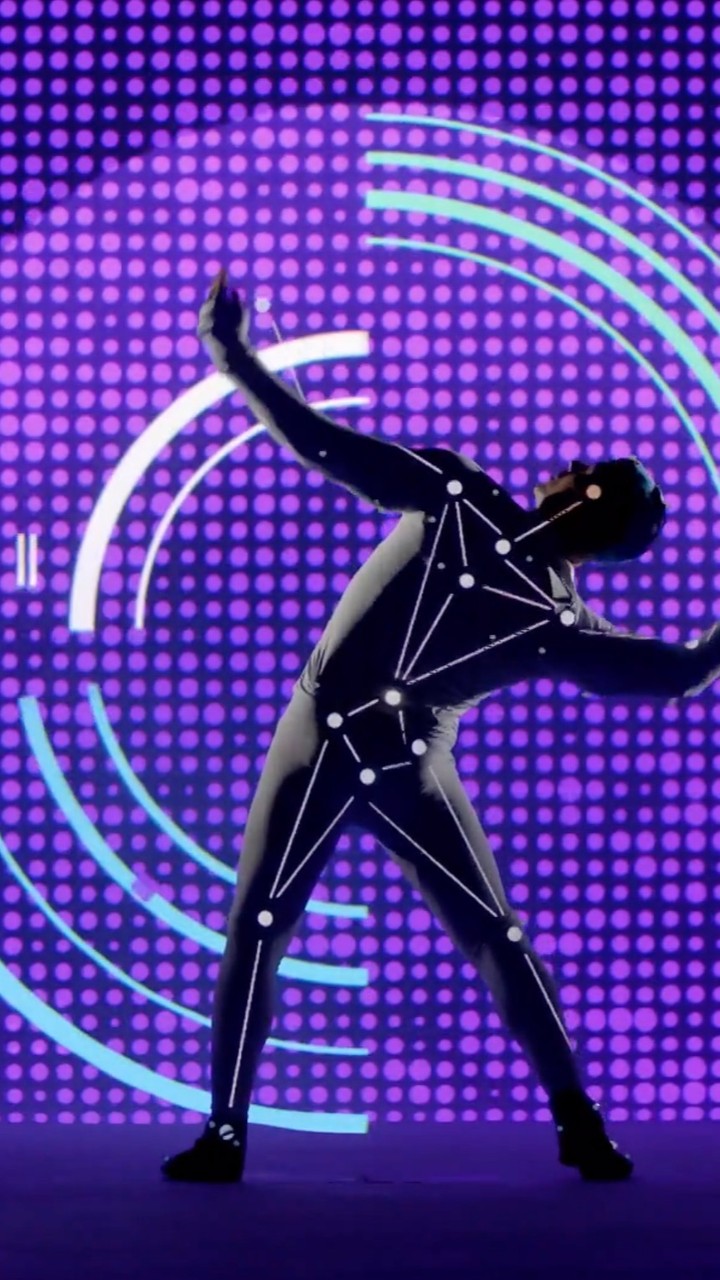 Full-body shot of adult wearing motion capture suit against purple dot background with teal lines. Motion capture suit with white dots.