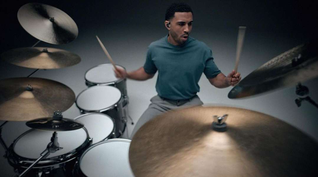 Man playing drums in a studio. A drummer with drumsticks is surrounded by drums and cymbals. The musician is wearing a t-shirt and pants.