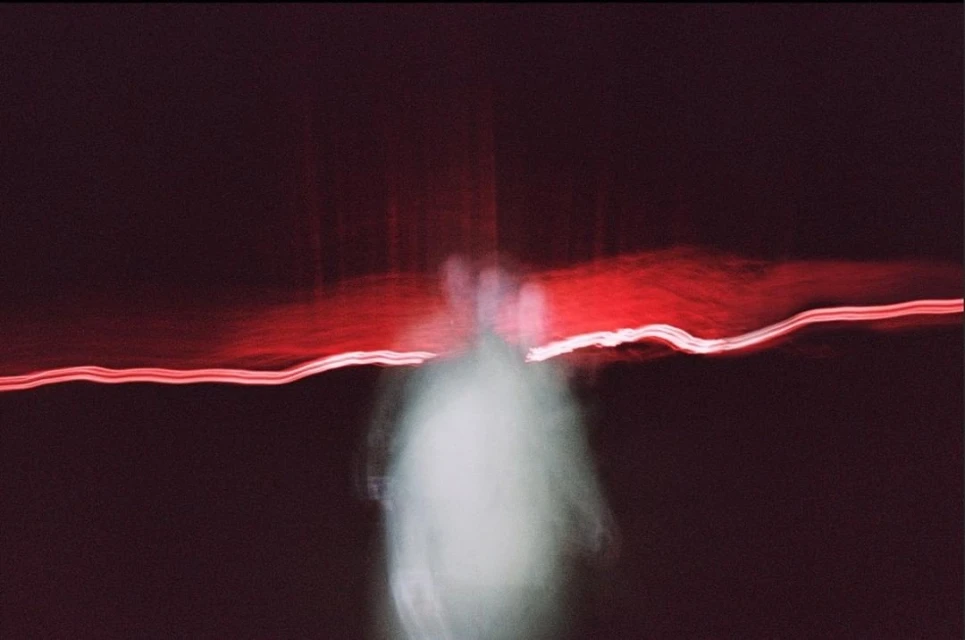 Abstract long exposure shot with blurred figure, red light streaks, and dark background, creating a mysterious and ethereal aesthetic.