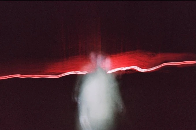 Abstract long exposure shot with blurred figure, red light streaks, and dark background, creating a mysterious and ethereal aesthetic.