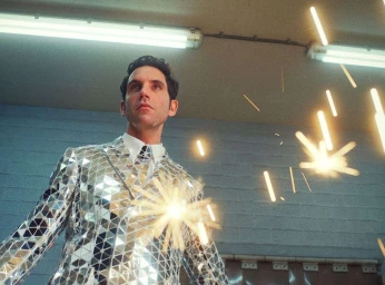 Man wearing a reflective mirror mosaic suit standing under fluorescent lights with bright glowing sparks flying around him.