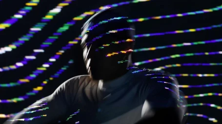 A person in a light-colored shirt captured with motion blur against curved rows of colorful glowing light trails.