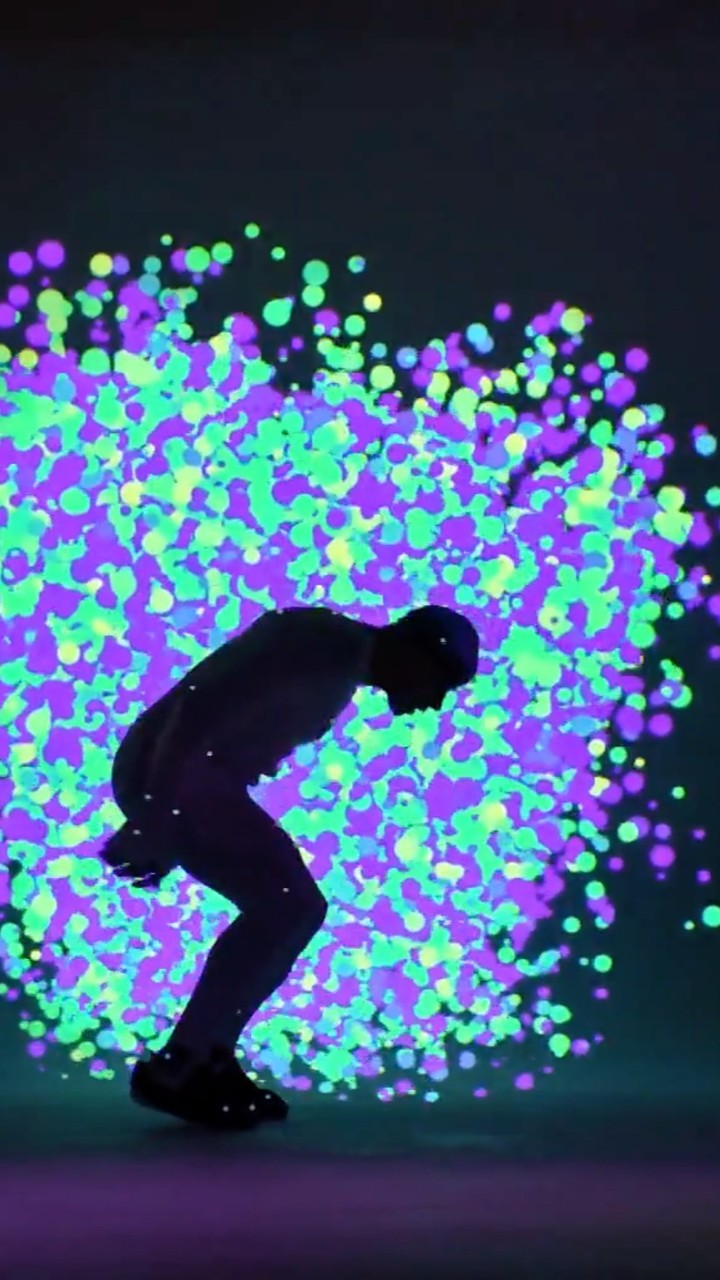 Silhouette of a man crouching against an illuminated backdrop of glowing purple and green dots.