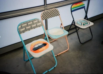 Three custom decorated folding chairs featuring unique graphic designs on seats and backrests in a New York studio setting.