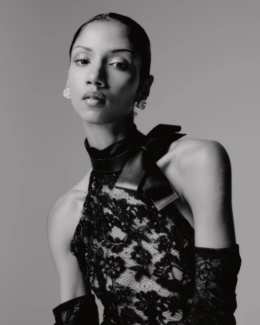 Black and white portrait of a woman in a lace dress with a high collar and bow detail, accessorized with earrings and gloves.