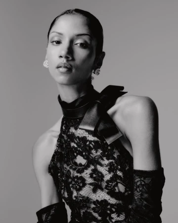 Black and white portrait of a woman in a lace dress with a high collar and bow detail, accessorized with earrings and gloves.