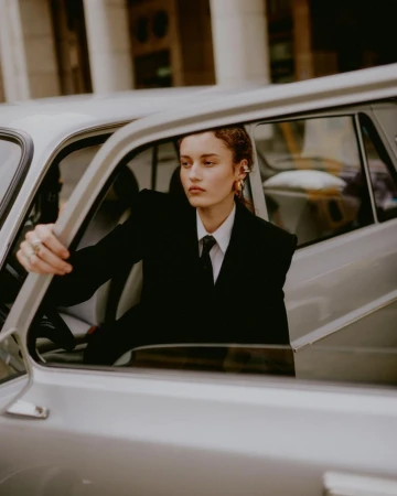 Woman in a black suit jacket and white shirt sitting inside a vintage silver car, photographed by Federico Barbieri in Milan.