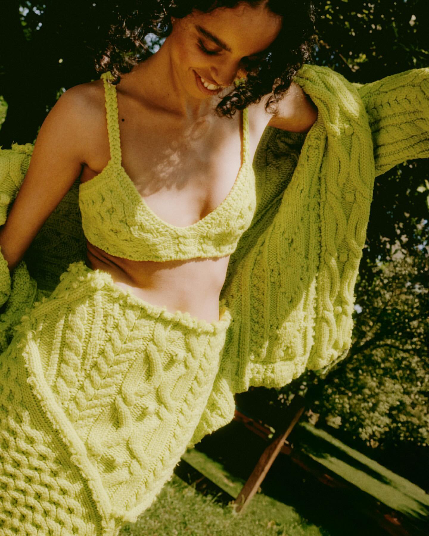 Smiling woman wearing a lime green knit bralette and matching cardigan outdoors in sunlight by Federico Barbieri