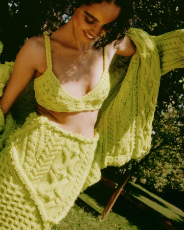 Smiling woman wearing a lime green knit bralette and matching cardigan outdoors in sunlight by Federico Barbieri
