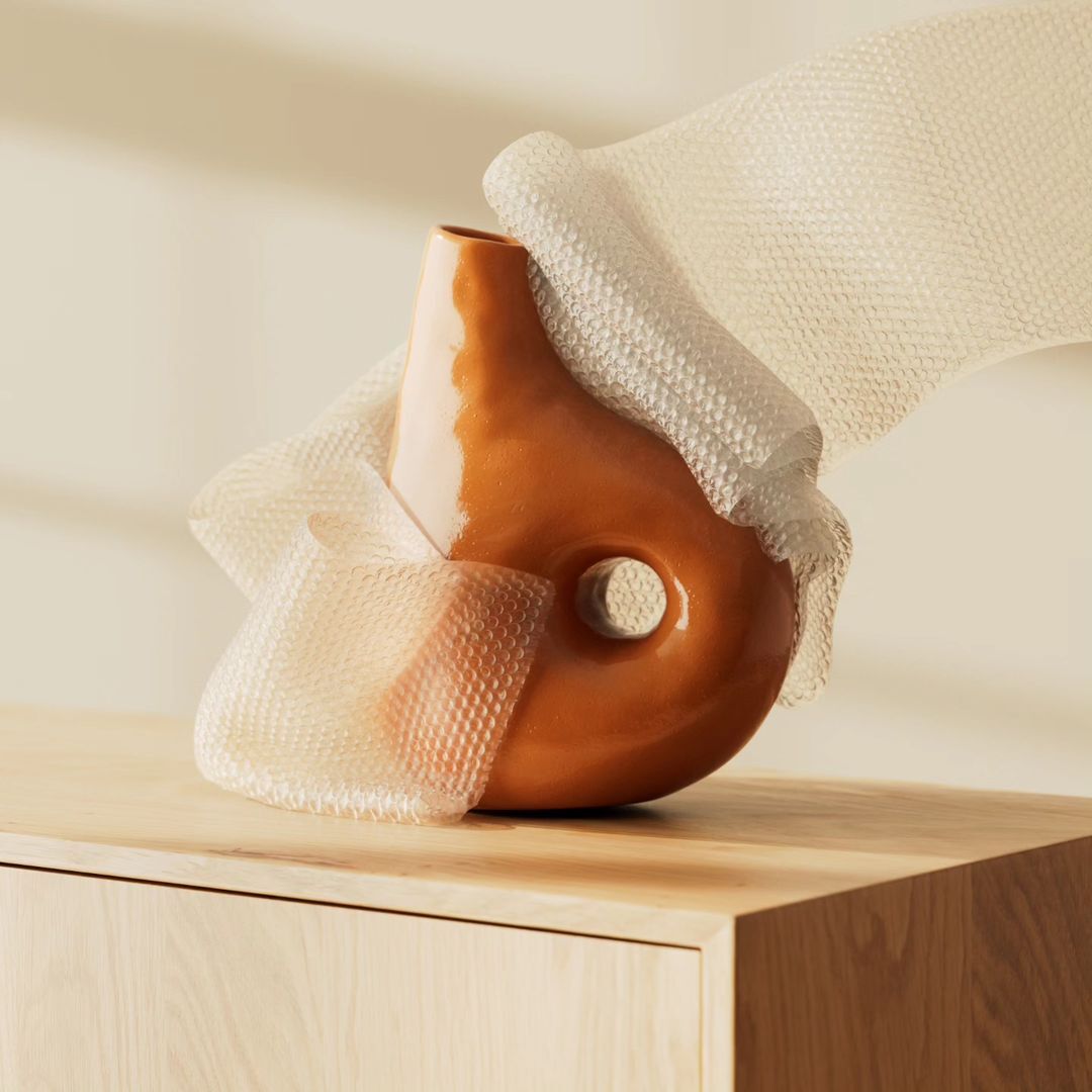 Orange ceramic vase on a wooden surface with bubble wrap around it, illuminated by soft lighting, casting a subtle shadow against a neutral background.