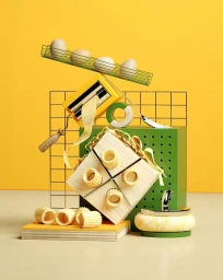 Balanced still life arrangement of pasta, eggs, a paint roller, and geometric blocks against yellow and beige surfaces.