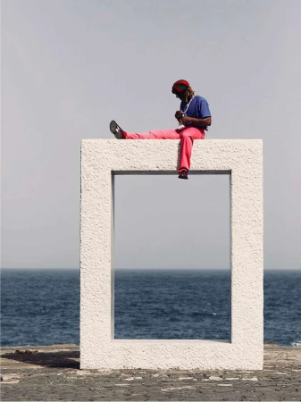 Man sitting on a large white stone frame overlooking the ocean by Fee-gloria Gronemeyer