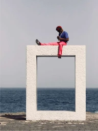 Man sitting on a large white stone frame overlooking the ocean by Fee-gloria Gronemeyer